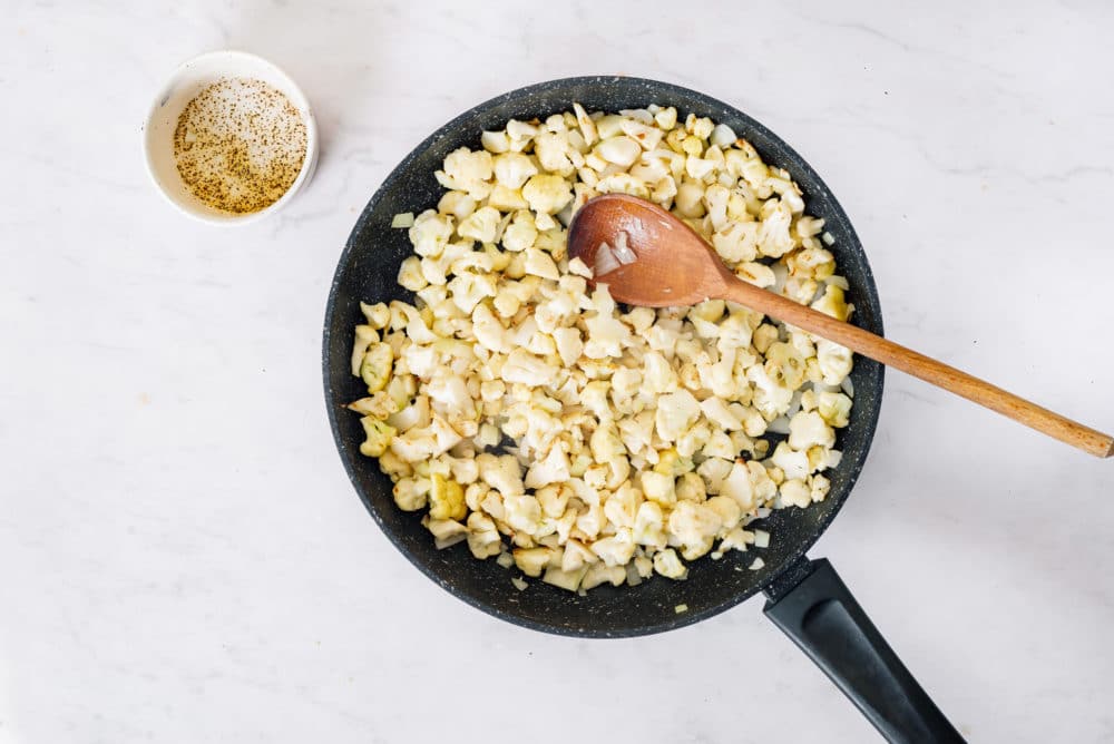 Cauliflower sauteing in a skillet with a bowl on the side.