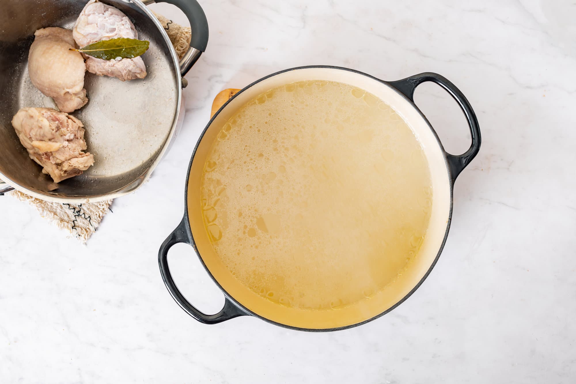 soup-pot-with-broth-in-it-and-a-silver-pot-with-chicken-and-a-bay-leaf-on-the-side