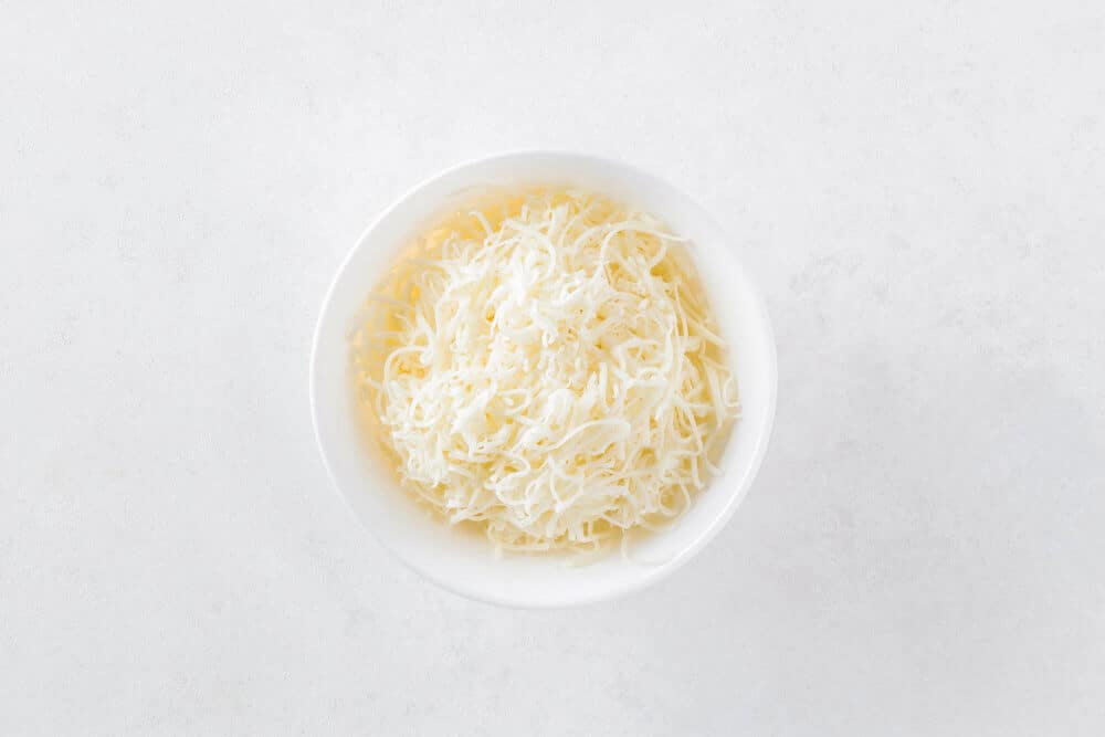 Shredded cheese in a white bowl.