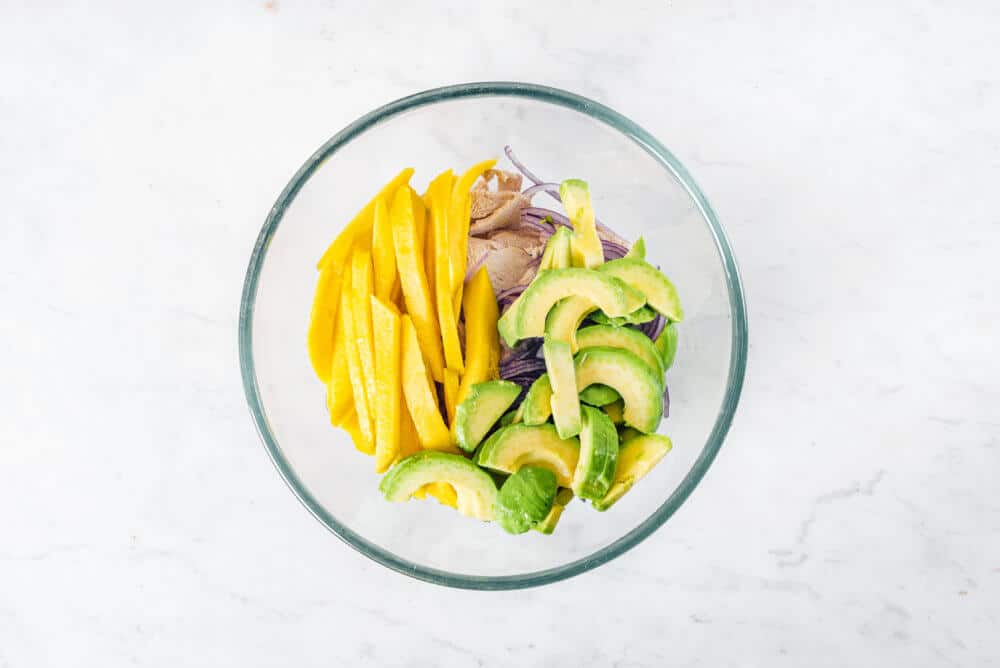 chopped mango and avocado added atop ingredients in a glass bowl.