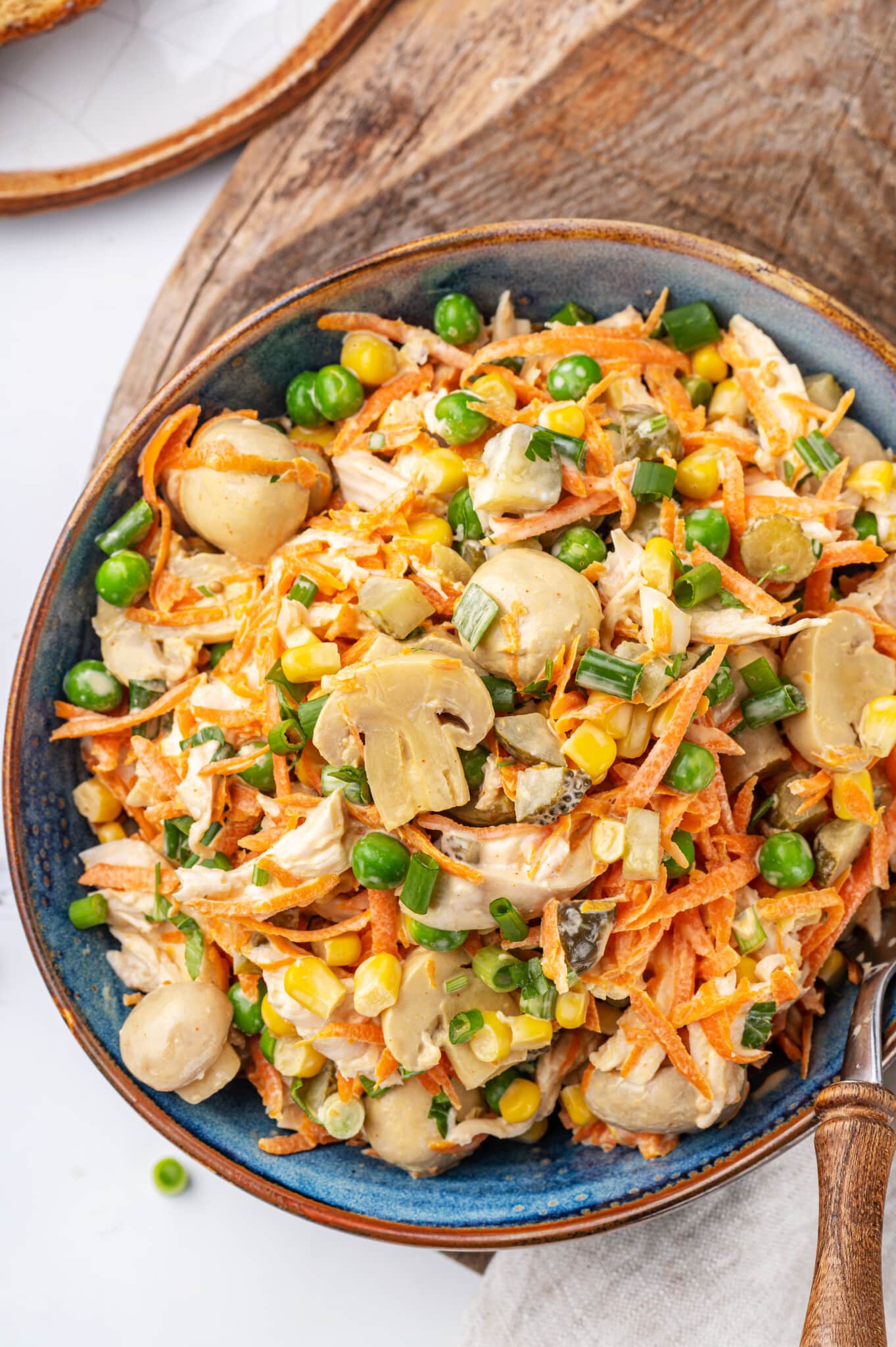 a blue bowl with a brown rim resting on a wooden board the bowl is filled with chicken mushroom veggie salad.