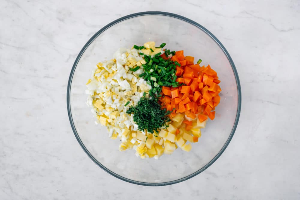 Chopped carrots, potatoes, greens, and eggs in a glass bowl.