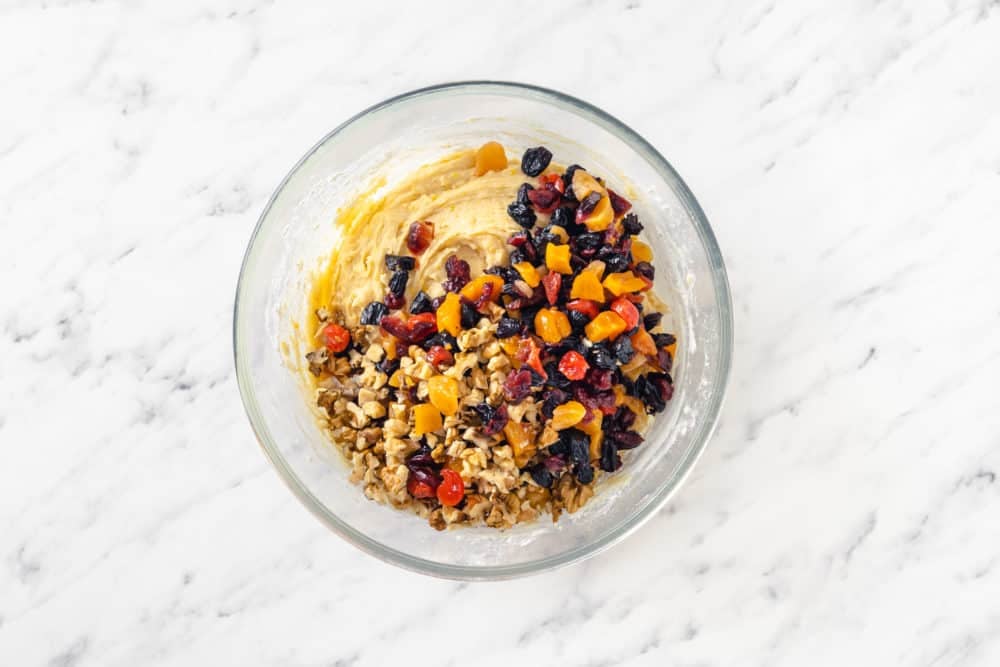 cake batter in a glass bowl with fruit cake filling on top nuts and dried fruits.