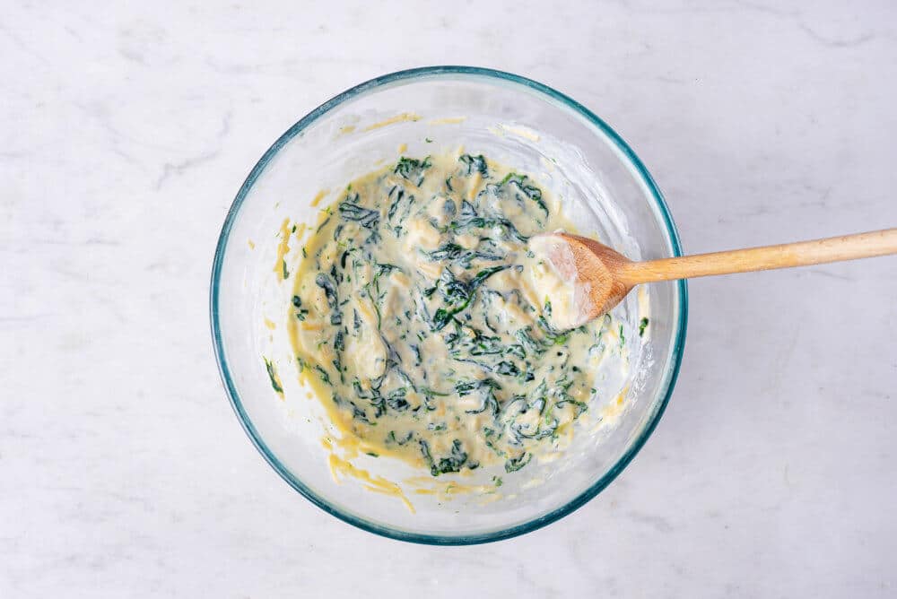 mixed filling made of spinach and other ingredients in a glass bowl with a wooden spoon.