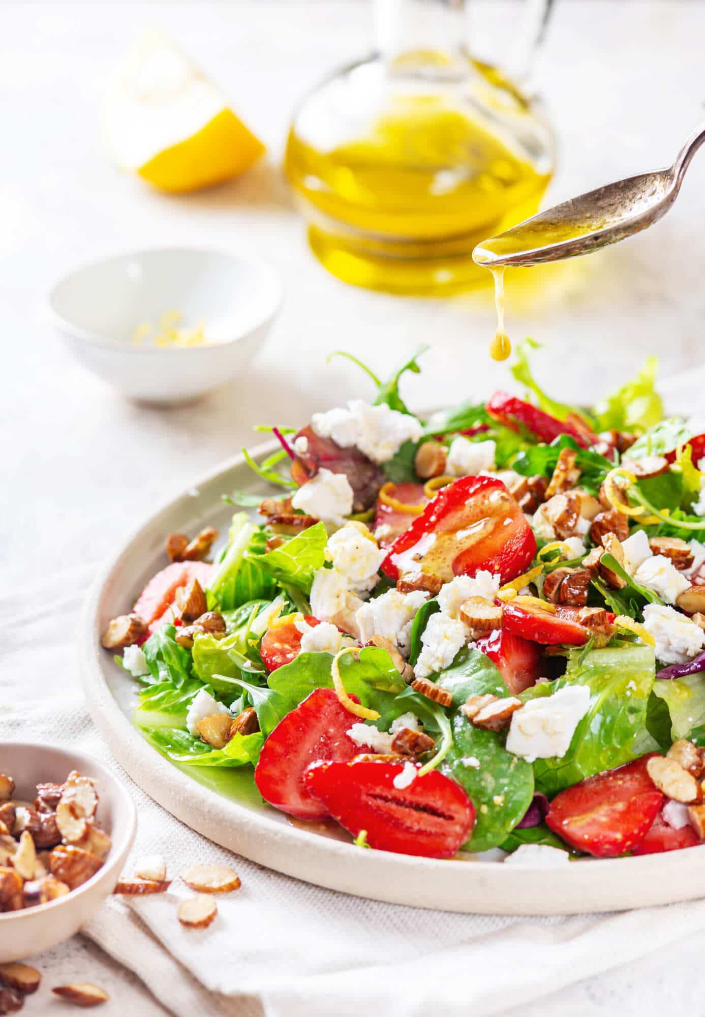 Summer berry salad on a white plate with dressing being poured on top with a spoon and olive oil in the background.