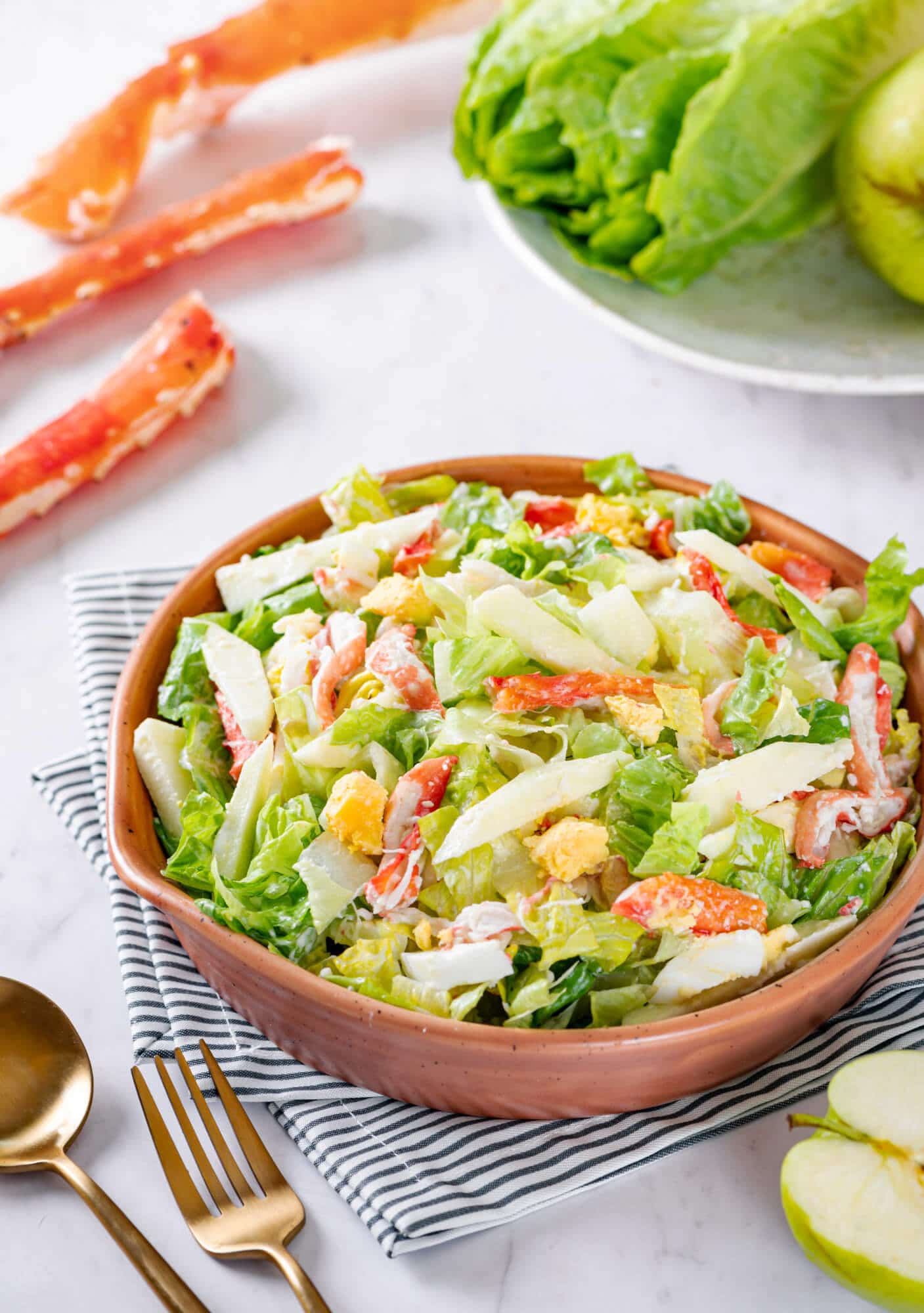 Crab apple salad in a brown bowl with 
 a gold fork on the side and crab legs in the background.