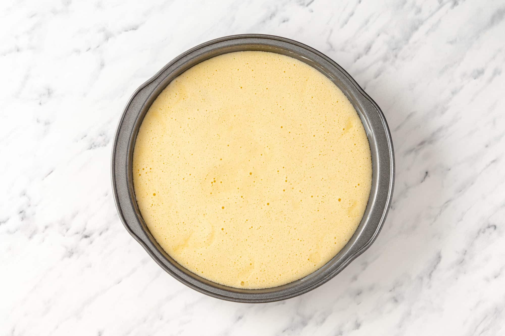 A grey 9-inch baking pan with cake batter poured in ready to bake.