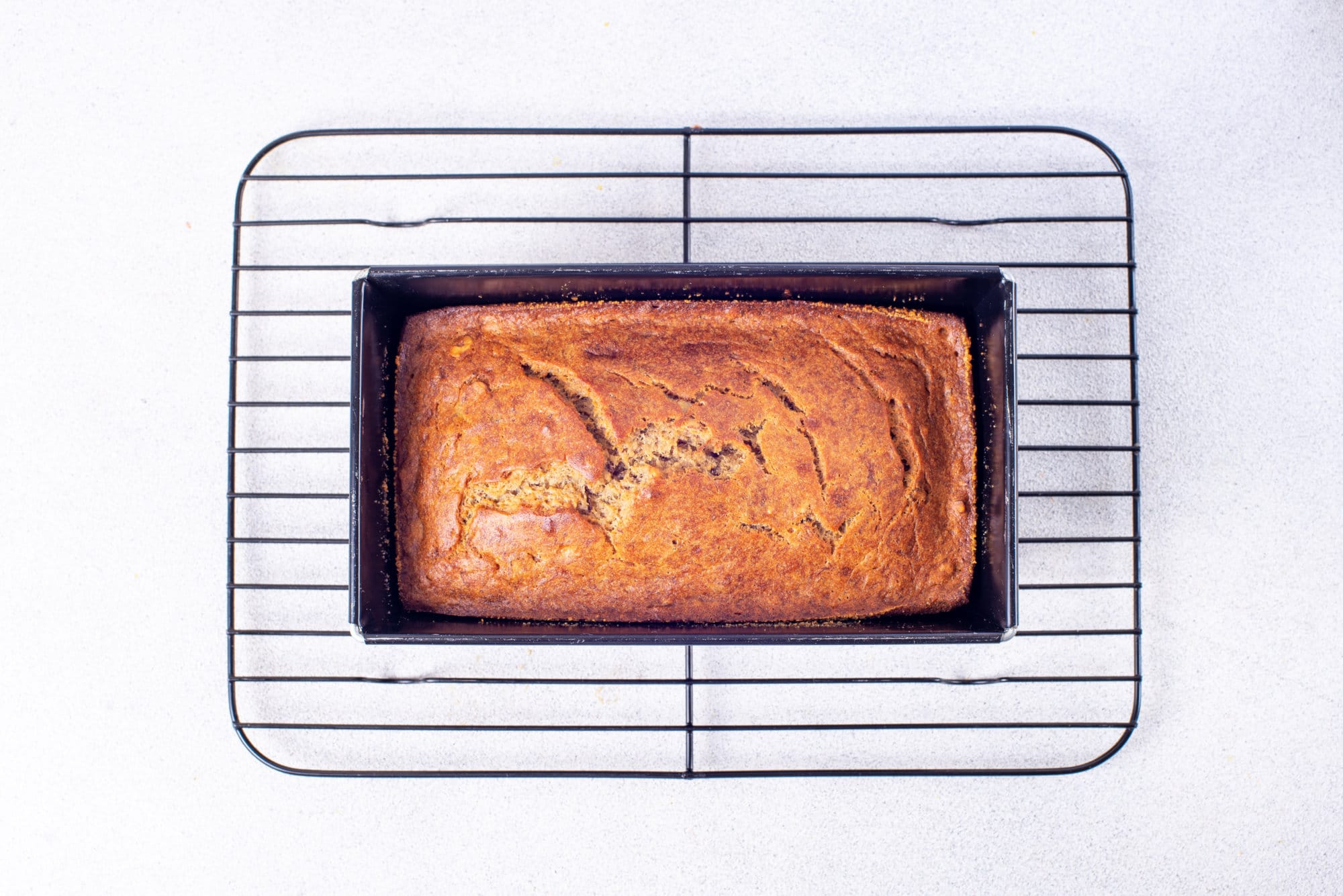 Baked banana bread in a loaf pan on a wire rack.