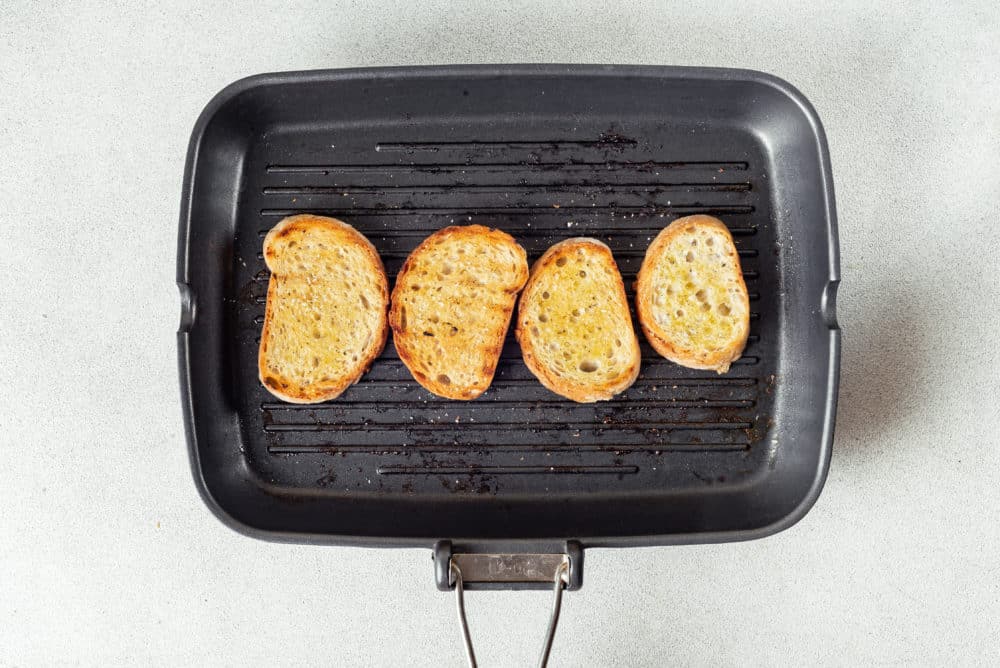 four slices of bread grilled on a black grill.