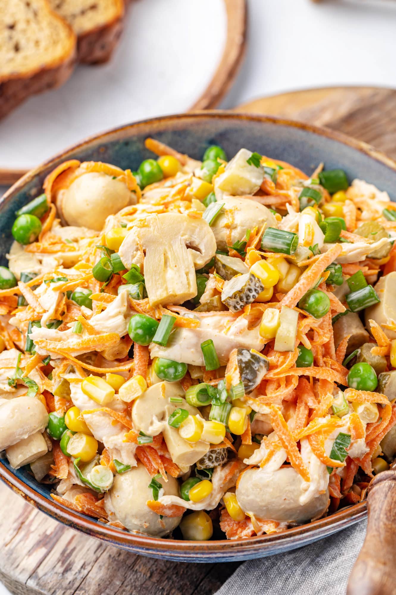 a blue and brown bowl filled with chicken veggie and mushrooms salad with a spoon on the side.