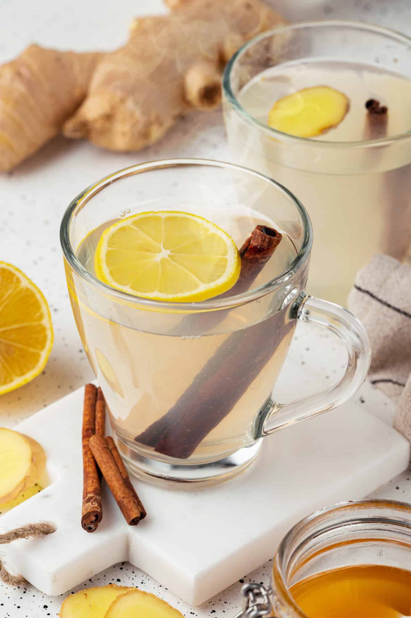 ginger tea in two glass mugs one on a white marble board with cinnamon sticks in the tea and on the board.