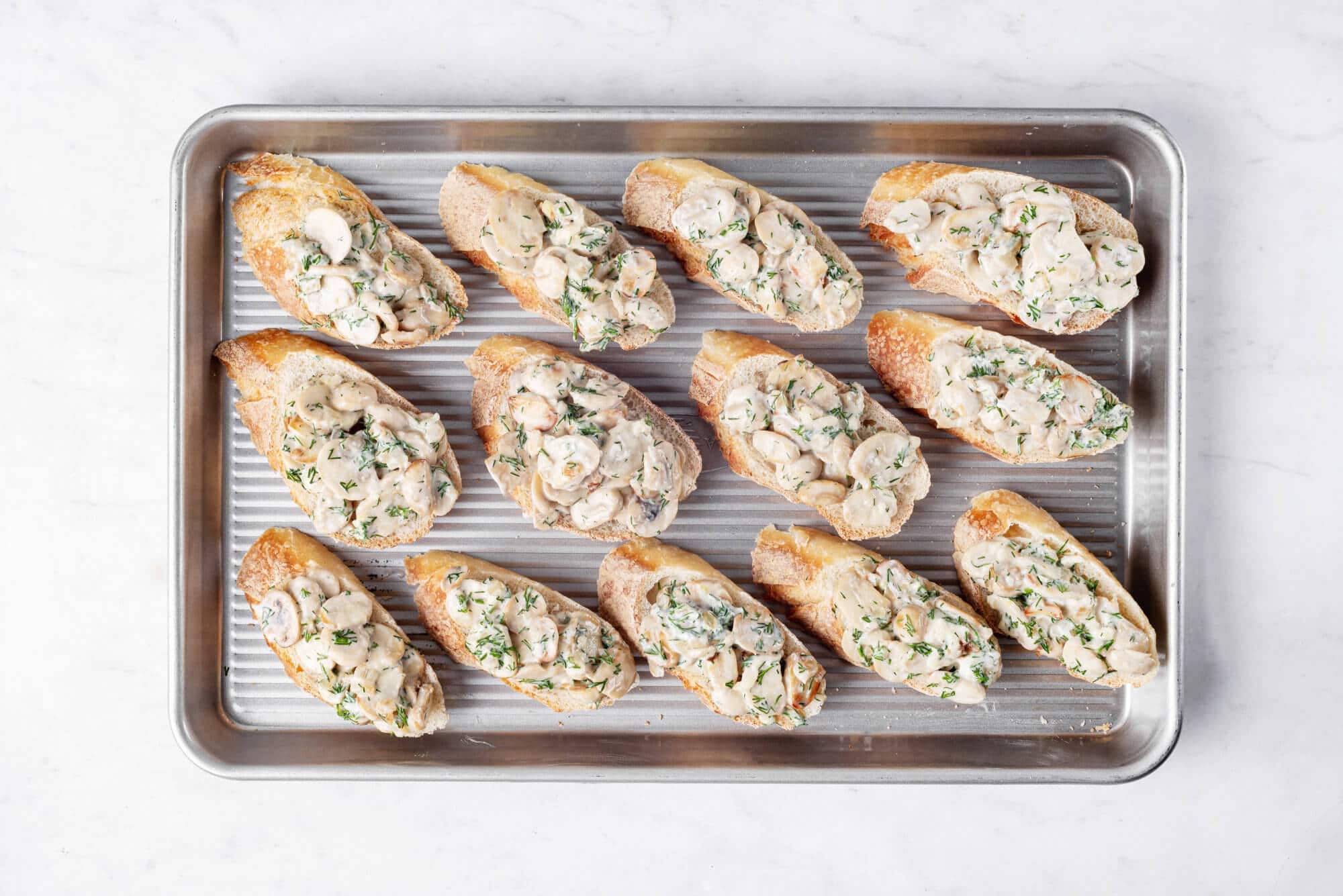 Mushroom mixture on baguette slices, on a baking sheet.