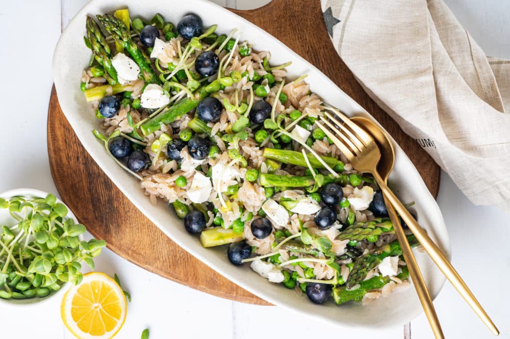 Mixed lemon orzo salad with blueberries in an oval white bowl with a fork and spoon on the side.