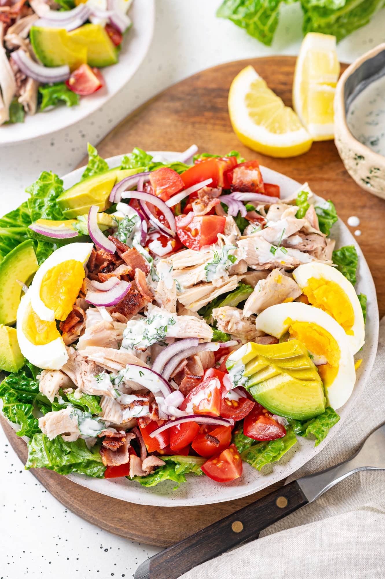 Chicken cobb salad on a white plate with lemon wedges on the side.