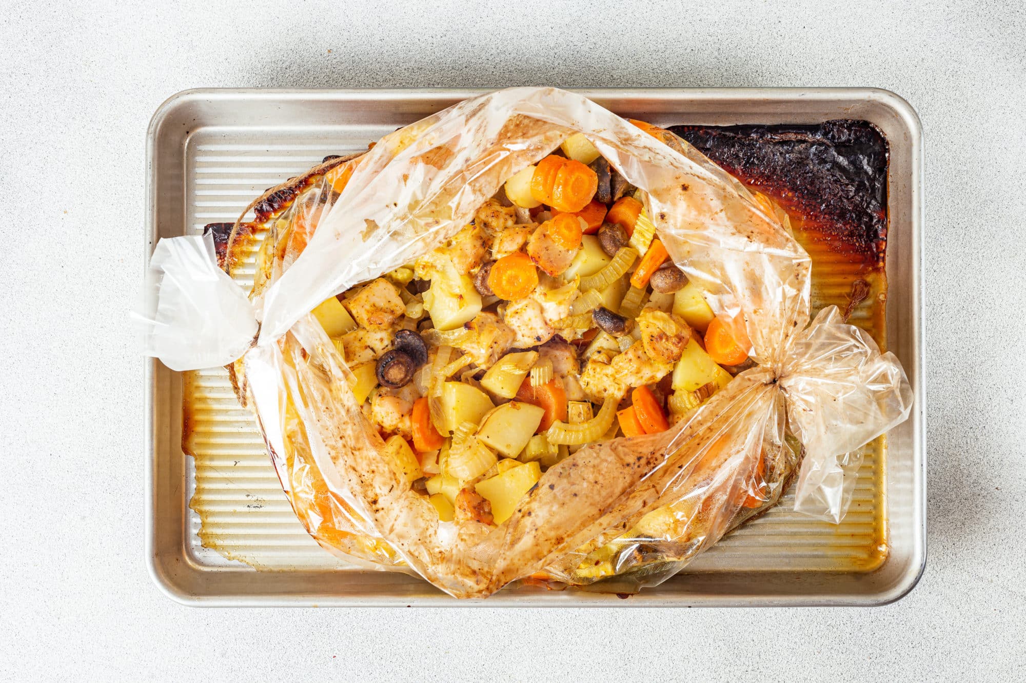 roasted chicken and veggies in an oven bag on a baking sheet.