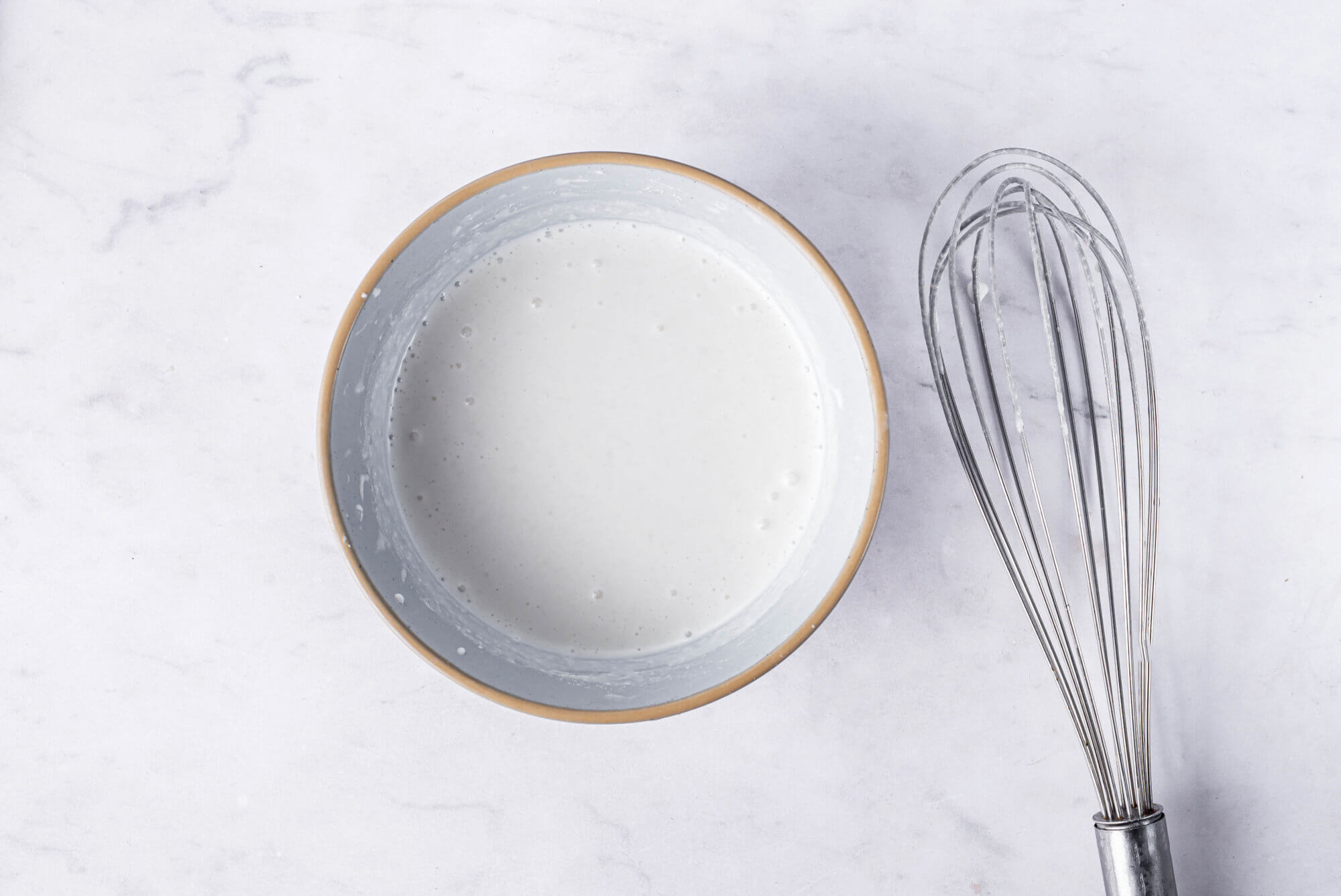 Heavy cream and flour mixed in a bowl with a whisk on the side.