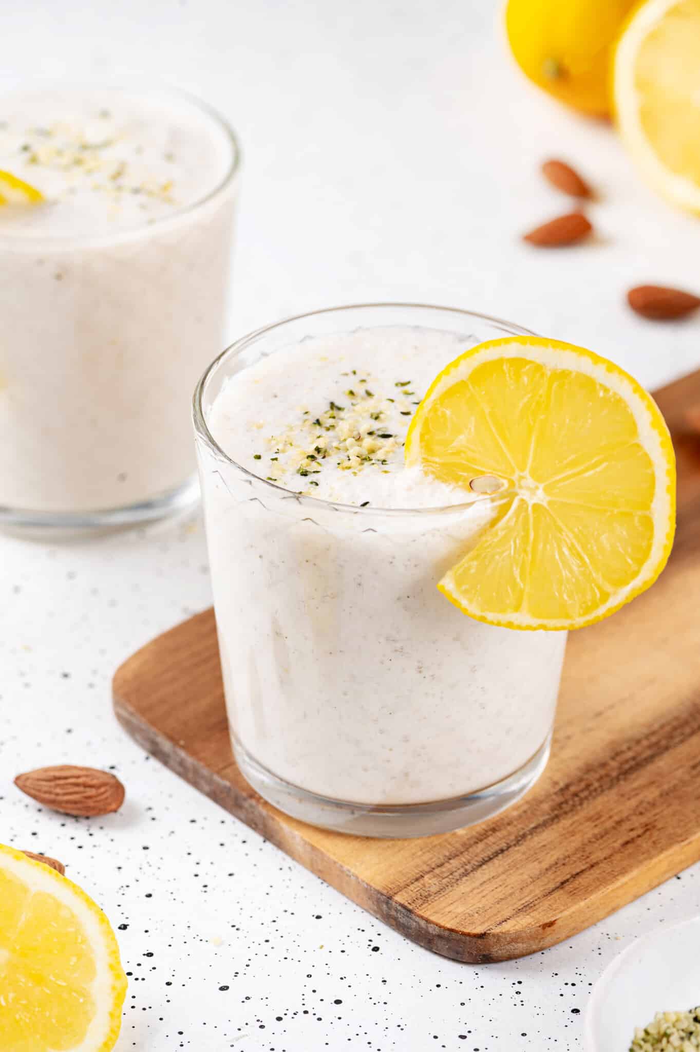 a glass of lemon smoothie with a lemon wedge on the rim with hemp seeds sprinkled on top.