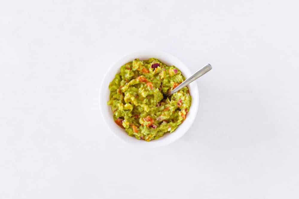 A white bowl of guacamole with a spoon in it.