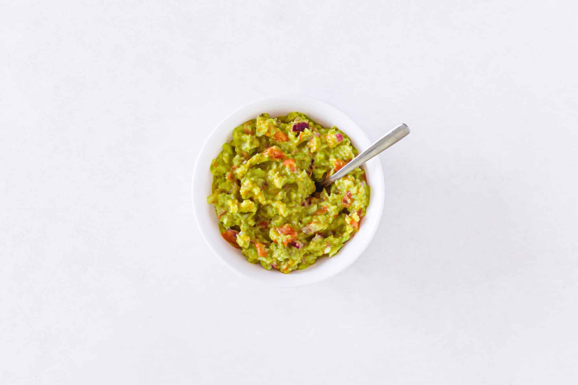 A white bowl of guacamole with a spoon in it.