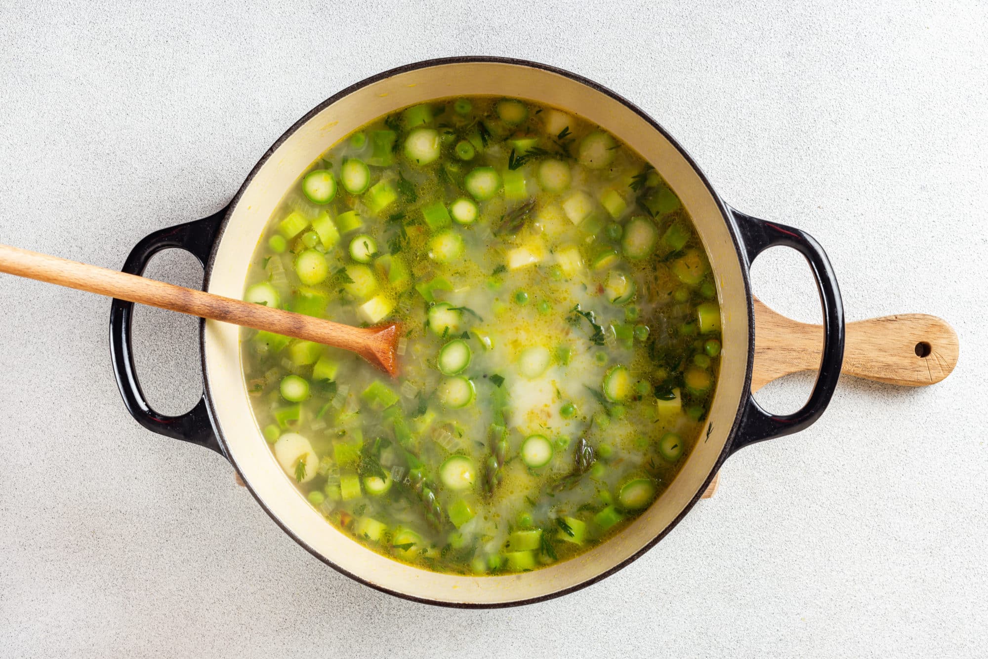 asparagus soup cooking in a pot with a wooden spoon.