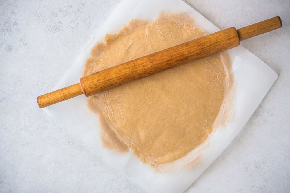 dough for an apple tart under parchment paper with a rolling pin on top.