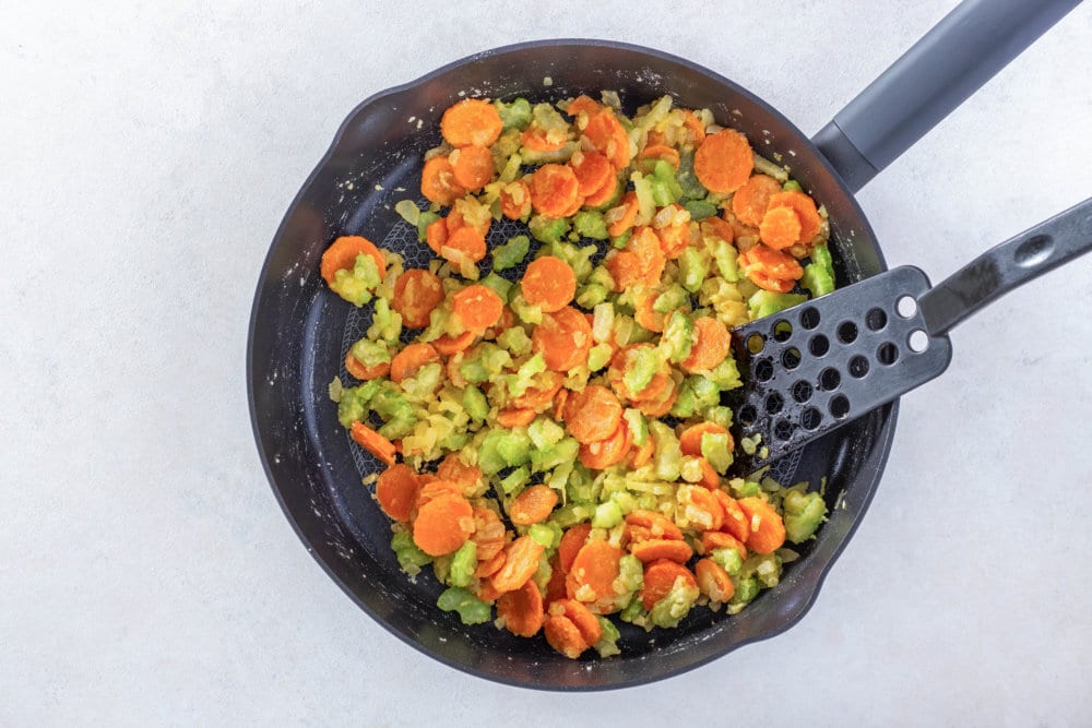 veggies sauteing in a skillet with a spatula.