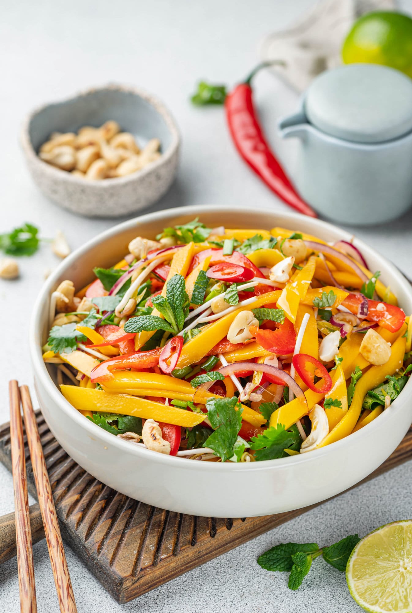 Thai salad in a white bowl on a wooden board with chopsticks on the side.