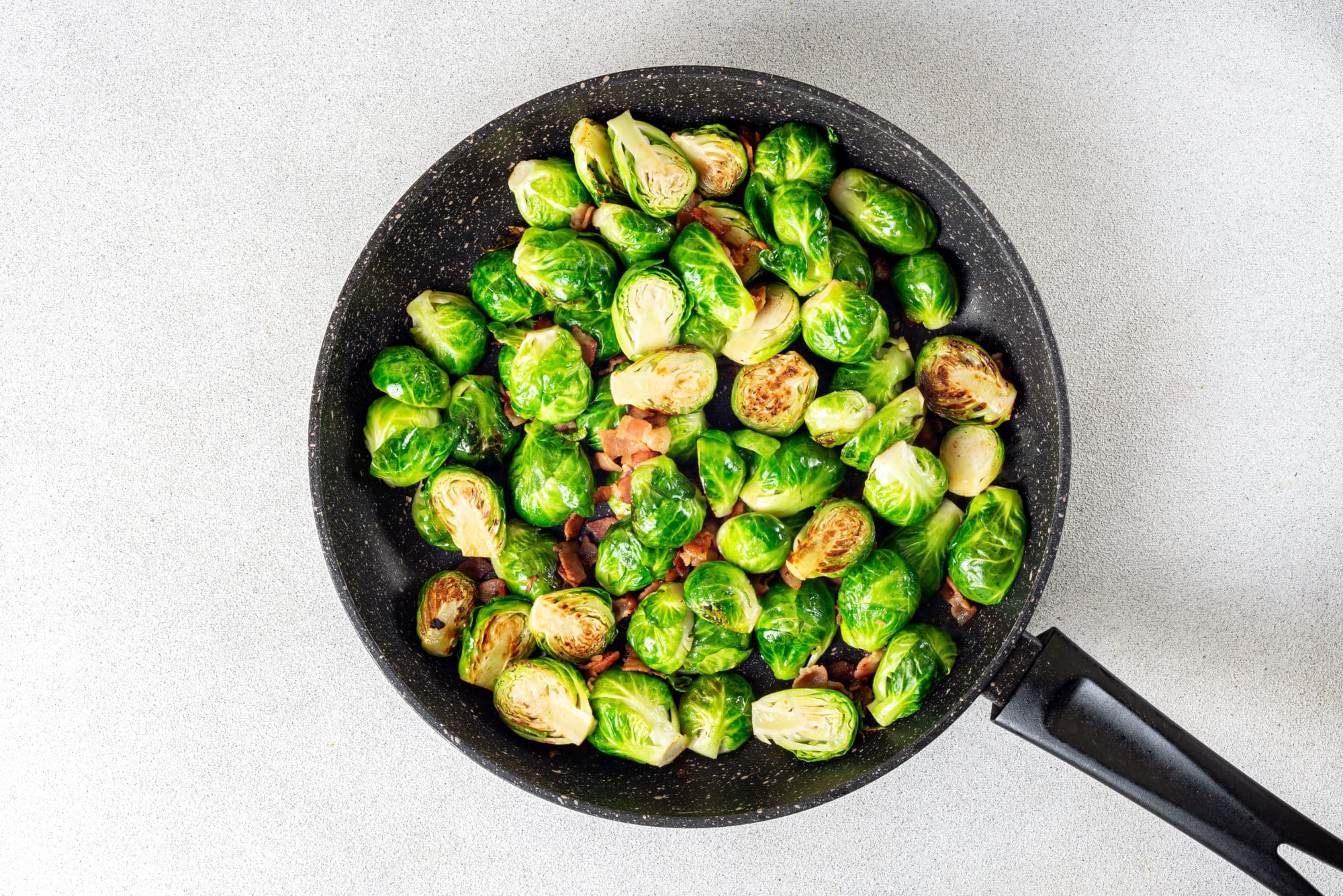 a black skillet with sauteed bacon and brussels sprouts in it.