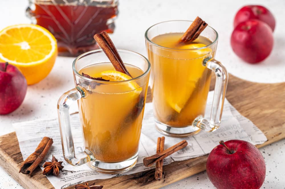 two mugs made of glass filled with apple cider and spices.