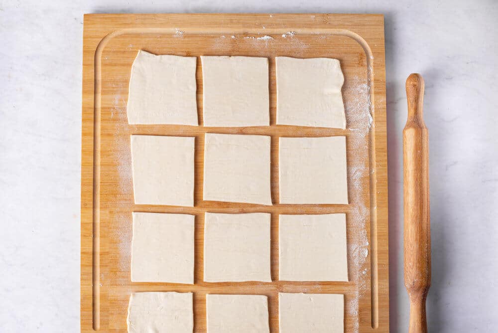 puff pastry spinach puffs on a wooden board with flour and a rolling pin.