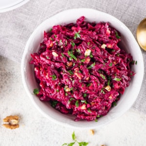 Beet salad in a white bowl with parsley sprinkled on top and a spoon on the side.