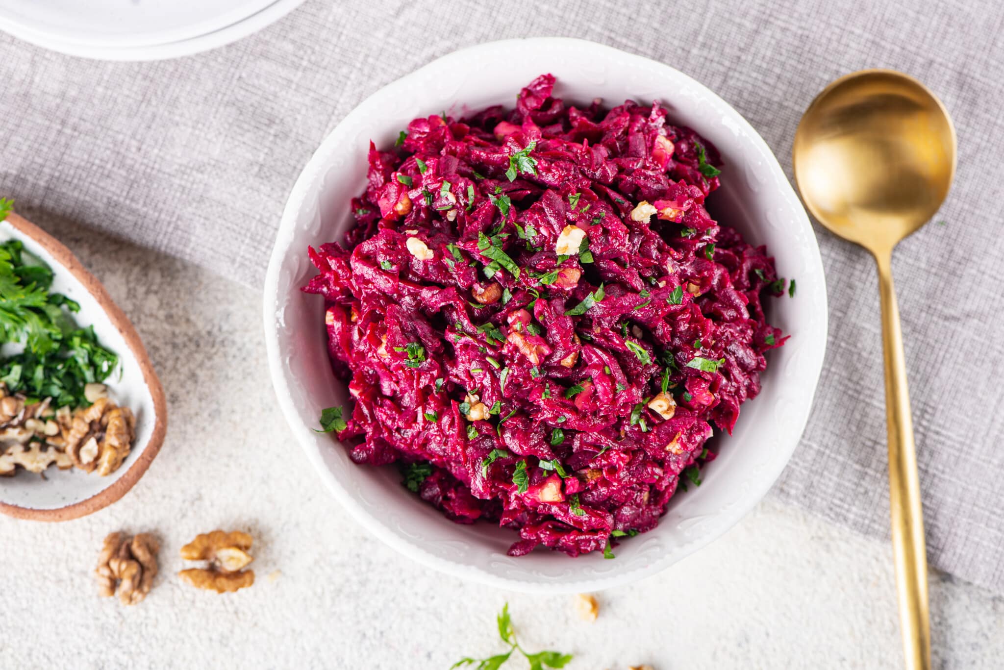 Beet salad in a white bowl with parsley sprinkled on top and a spoon on the side.