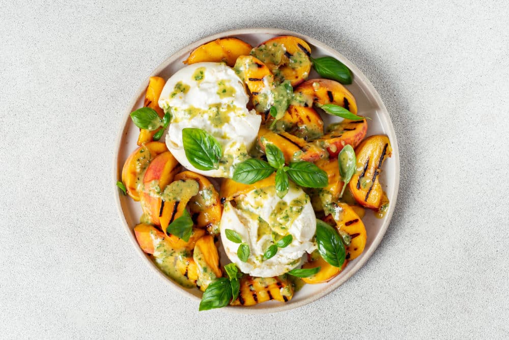 grilled peaches and burrata salad with basil and drizzled dressing on top.