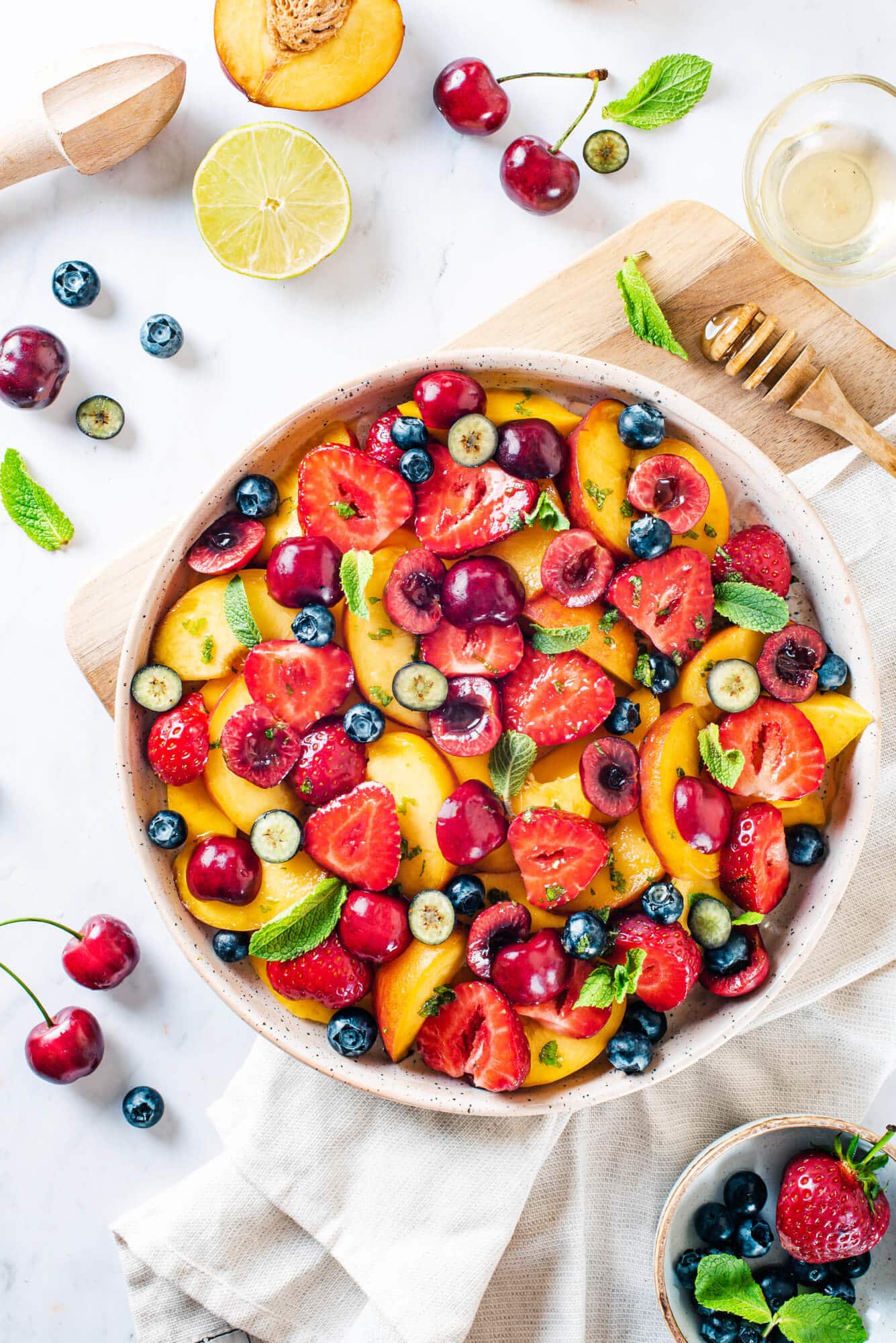 Summer fruit salad in a bowl with ingredients for the salad around.