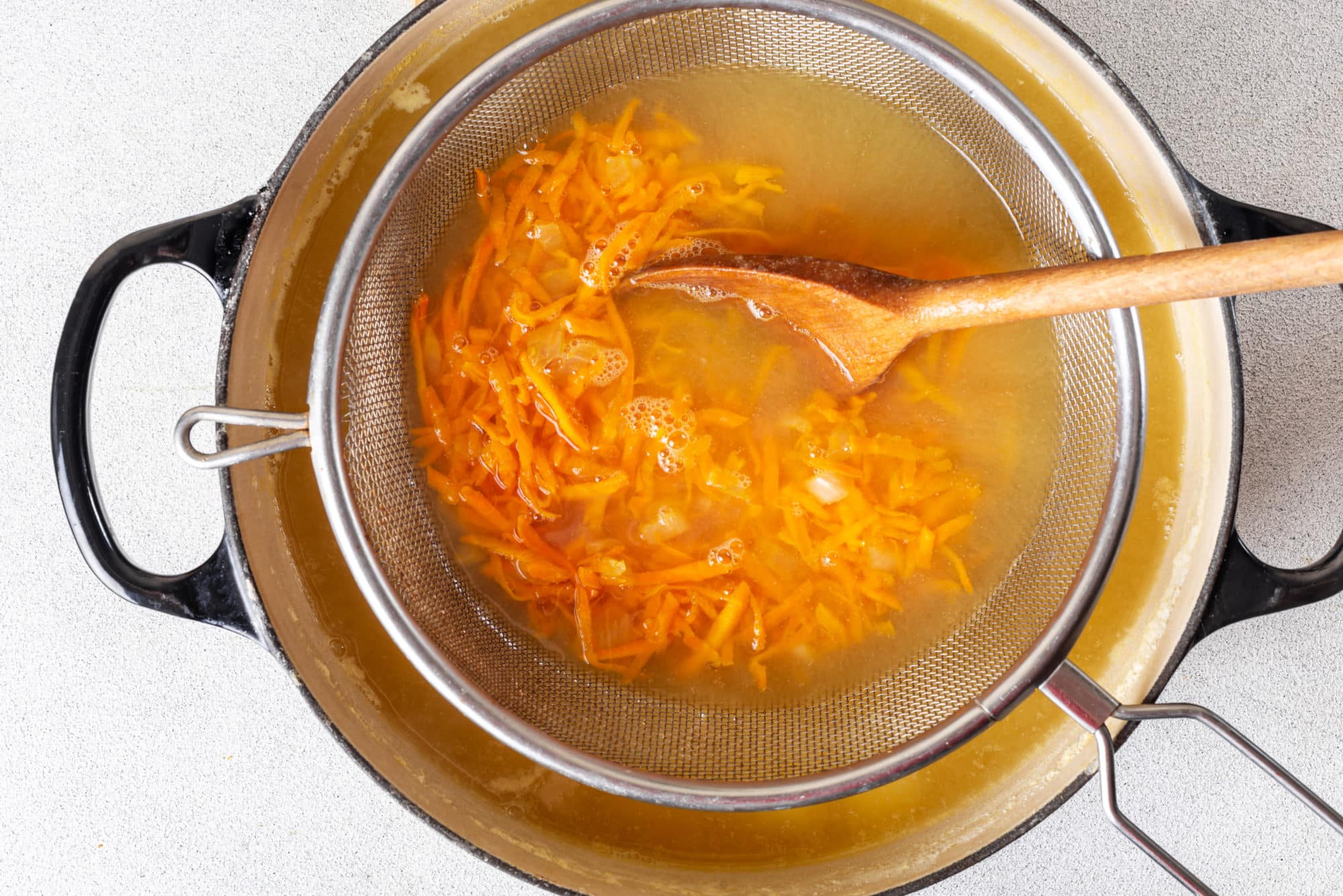 grated-carrots-in-a-sieve-over-the-soup-pot-with-split-pea-soup-in-it-with-a-wooden-spoon