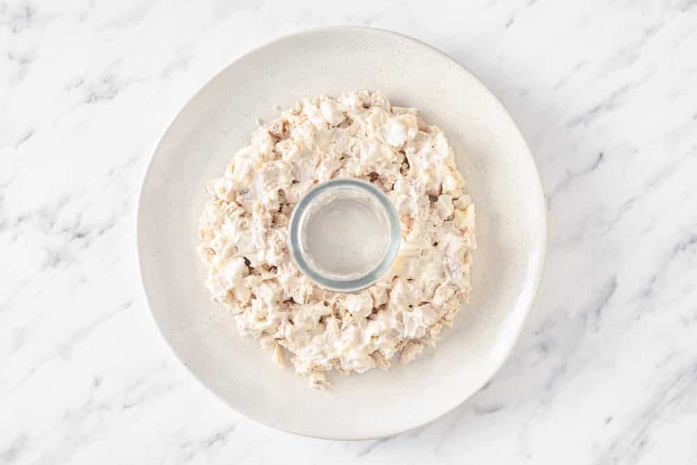 a white plate with a glass in the center creating a wreath shape for the chicken and mayonnaise salad layer on the plate.