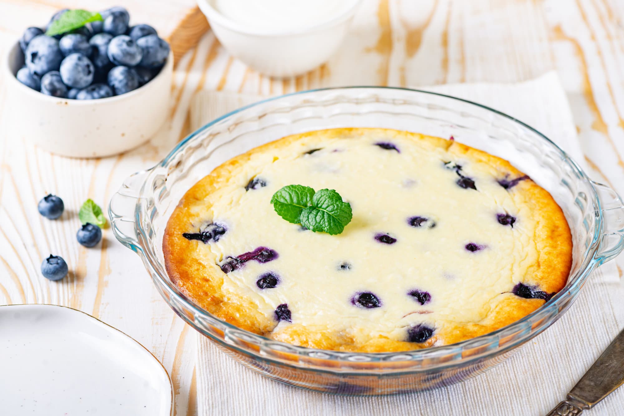 Blueberry cheese cake in a glass tray with a bowl of blueberries on the side.