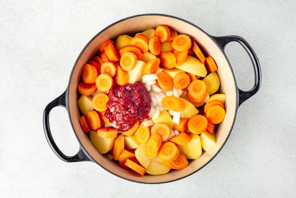 stew ingredients in a pot with tomato paste on top.