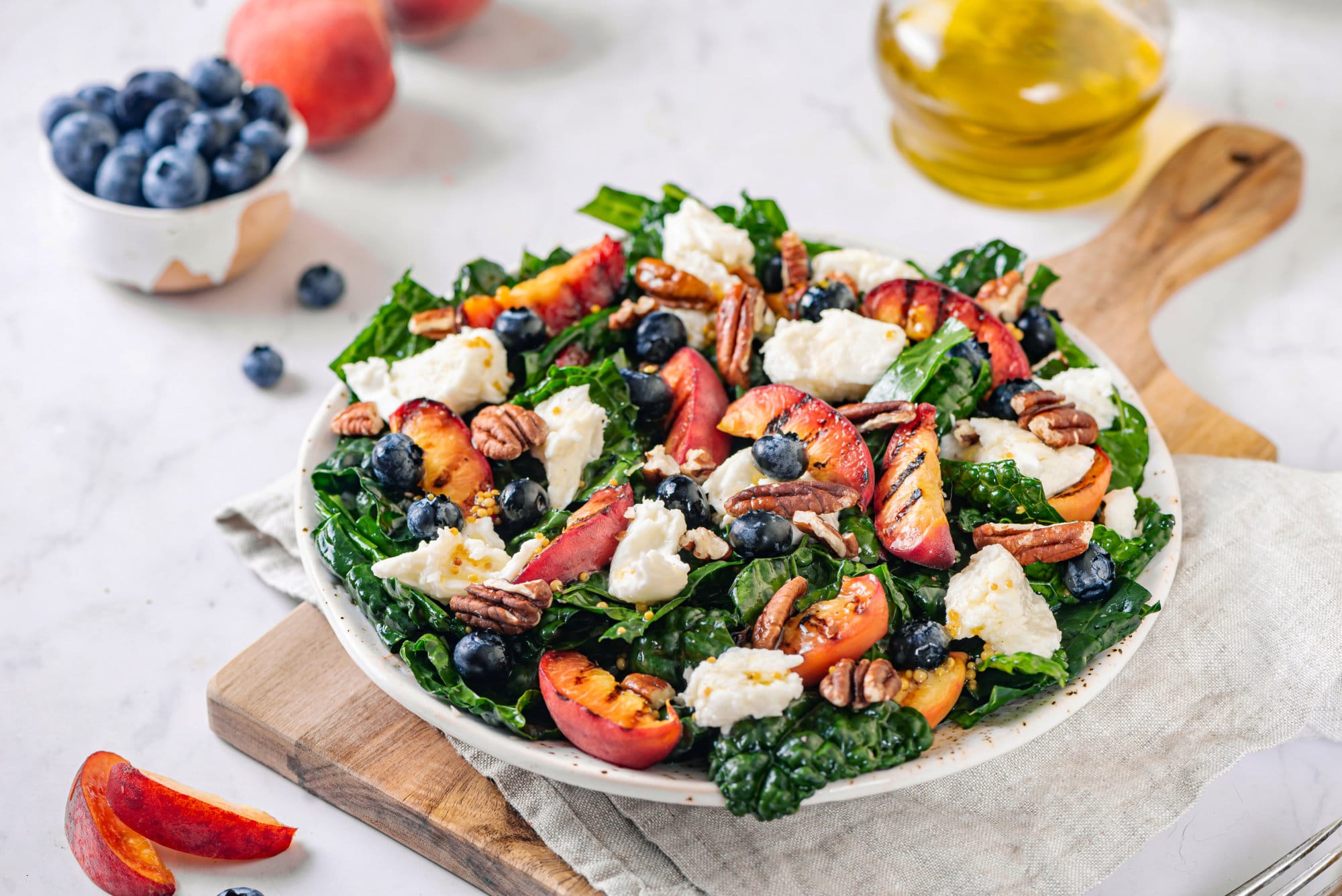 Peaches and kale salad on a white plate with mozzarella, blueberries, and pecans on top ready to serve.