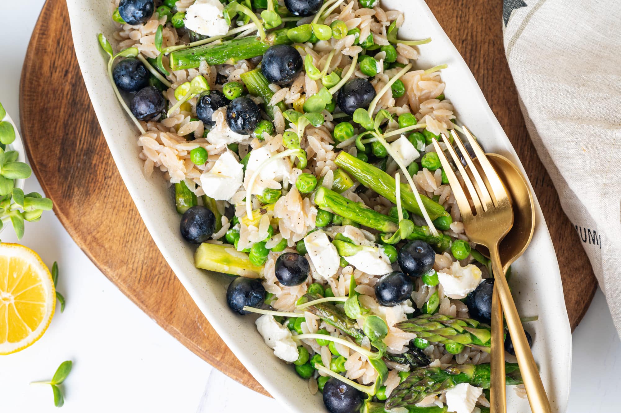 Orzo and lemon salad in a white oval shaped bowl with a fork and spoon in the bowl.