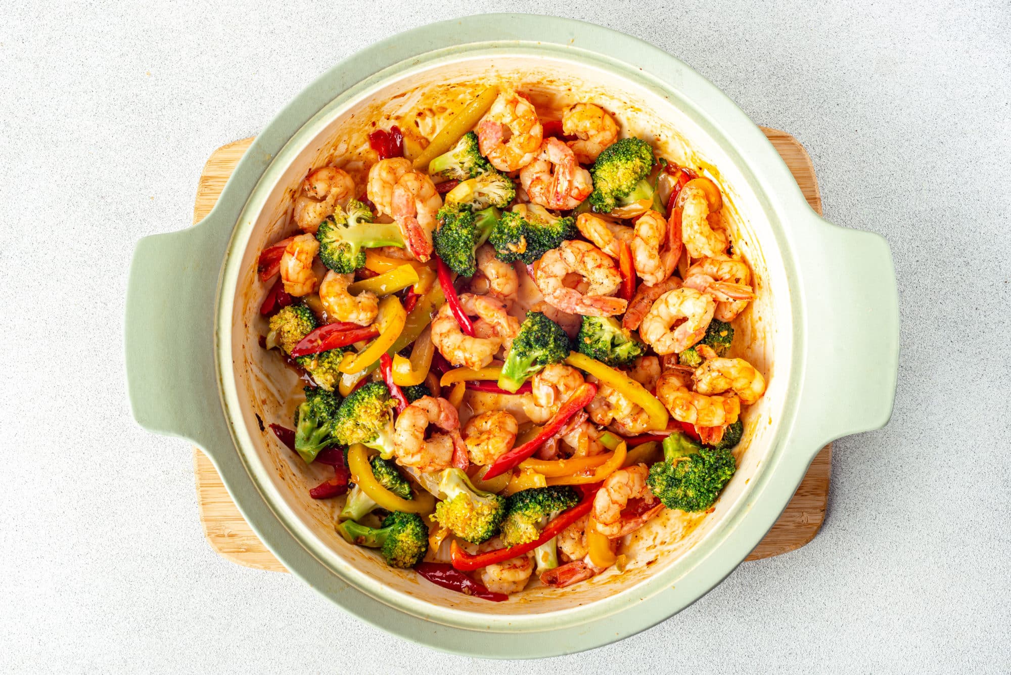 veggies and shrimp in a pot on a board.