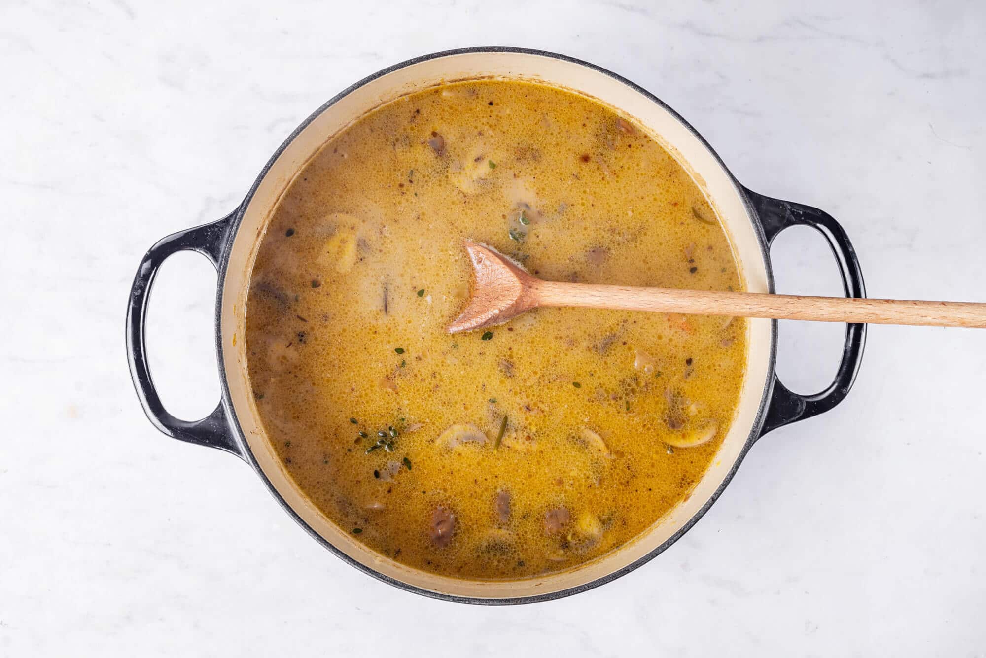 Making mushroom soup in a large black soup pot with a spoon.