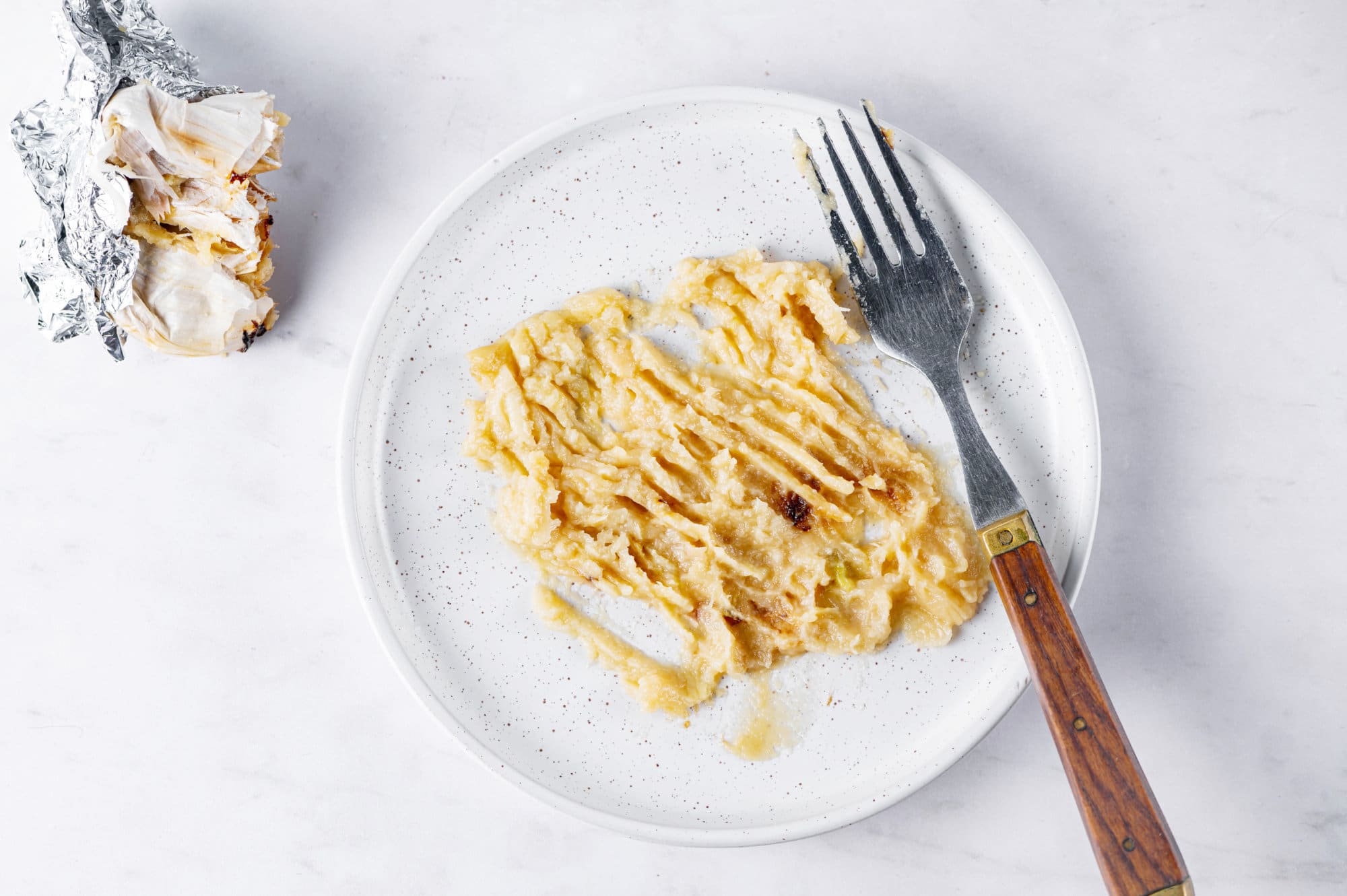 mashed garlic on a white plate spread out with a fork.