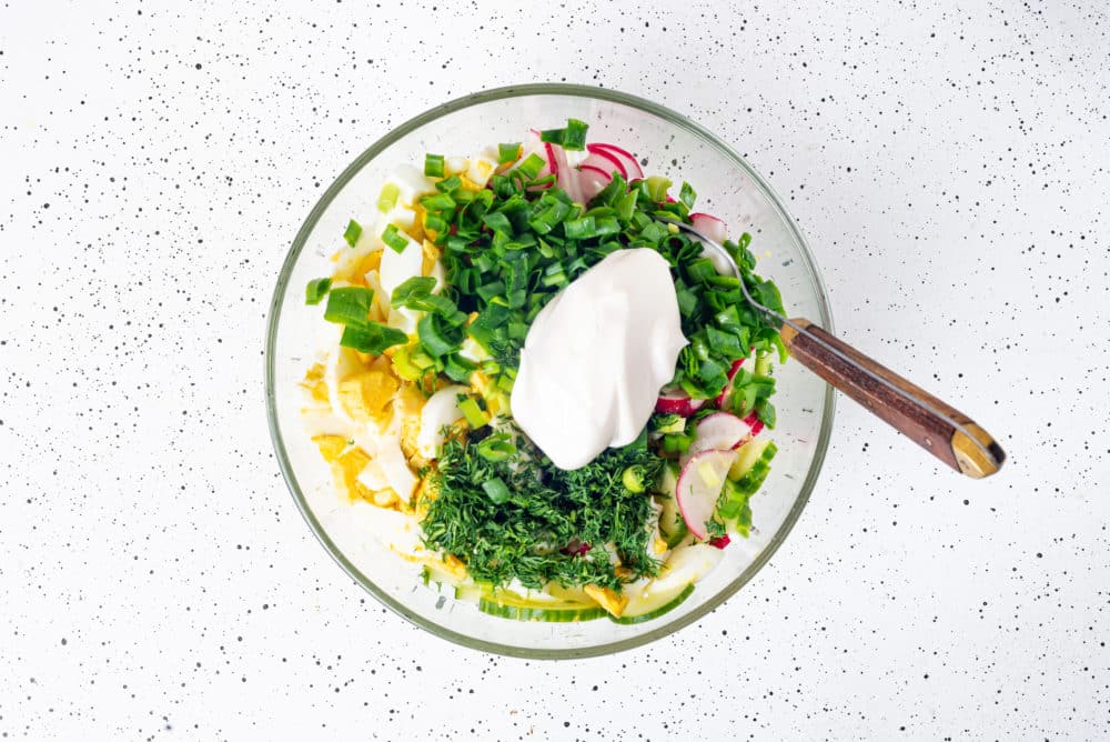 Salad ingredients in a glass bowl ready to combine with a spoon.