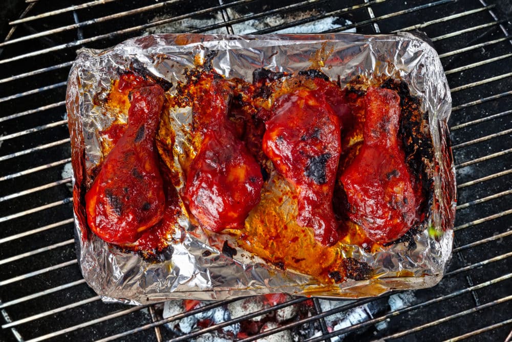 Chicken drumsticks cooking over a grill.