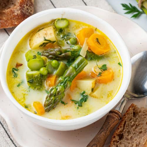 asparagus soup in a white bowl topped off with asparagus and carrot pieces.