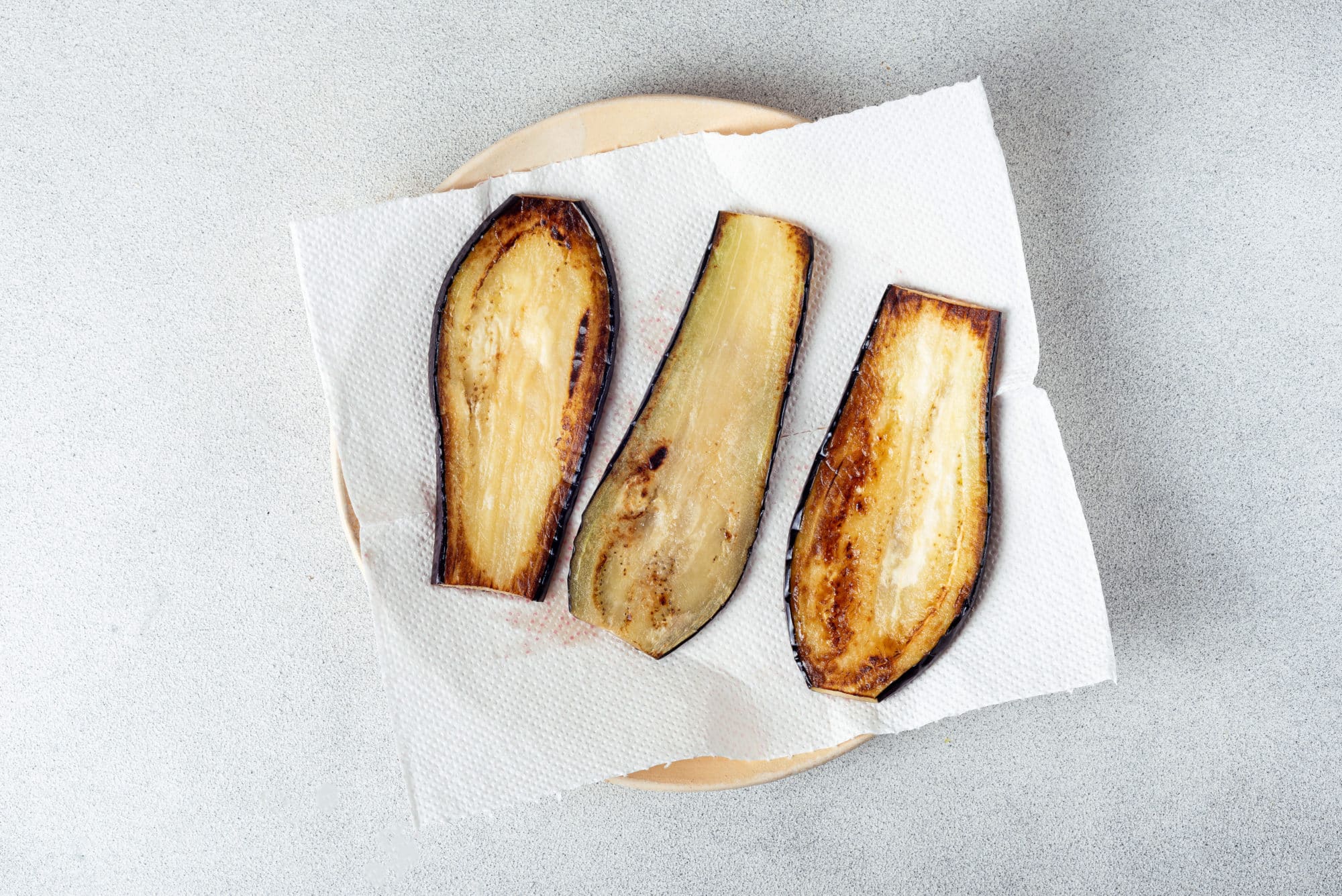 sauteed eggplant slices on a paper towel with a beige plate underneath.