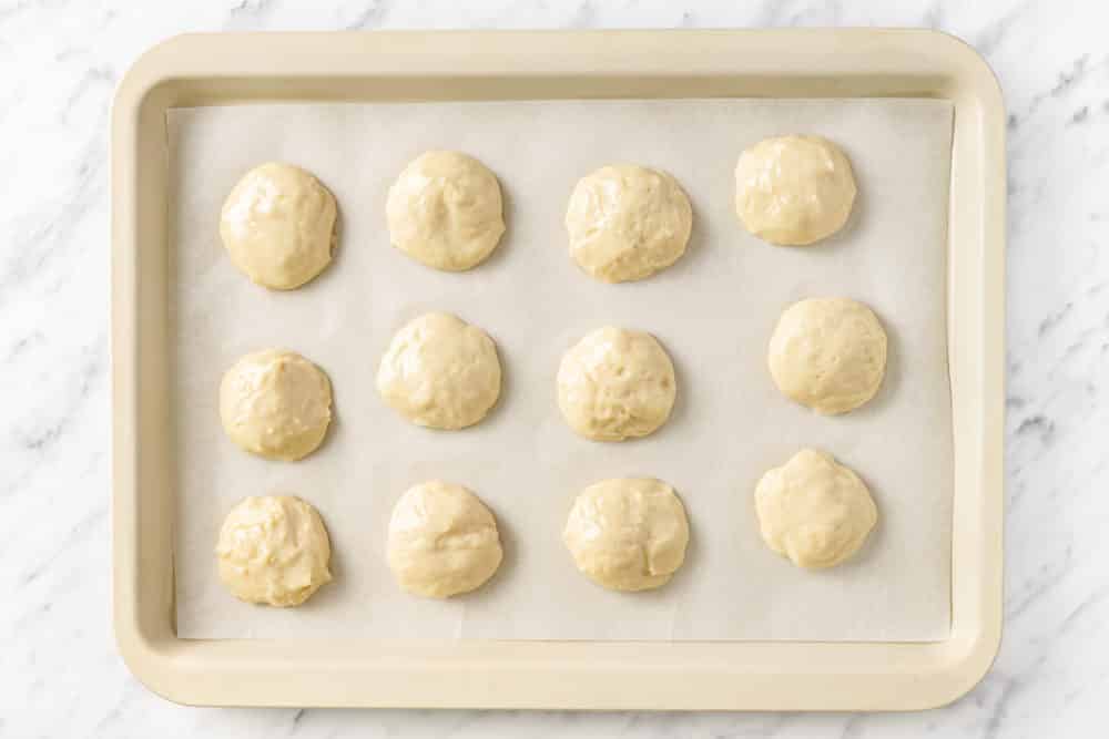 measured raw cookie dough separated on parchment paper on a baking sheet.