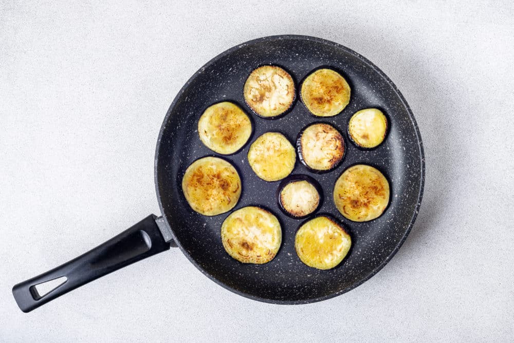 eggplant slices sauteing on a black skillet.