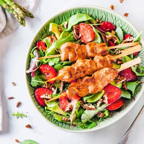 Chicken skewer salad in a bowl with chicken skewers atop a bed of greens.